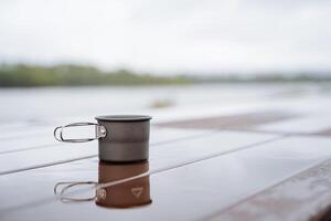 Aluminium Becher steht auf das Tabelle im ein Pfütze von Wasser, Betrachtung im das Wasser, Tee Glas, Kaffee Becher wandern, Reise zu Natur, Camping Essen trinken Tee foto