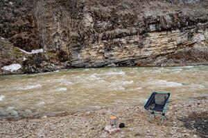 ein falten Stuhl steht allein auf das Bank von das Fluss. Camping Ausrüstung. falten Stuhl. foto