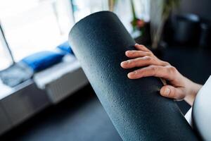 Nahansicht Yoga Matte. Blau ist ein Sanft Element von Sport Ausrüstung. das Hand hält das Yogakamerad gerollt oben im ein rollen. foto