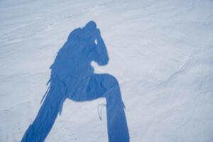 das Schatten von ein Mann auf das Weiß Schnee, ein Tourist klettert ein Berg, das Silhouette von ein Bergsteiger im sonnig Wetter. foto