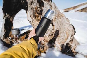 Thermosflasche zum Tee, halt im Ihre Hände ein Thermosflasche mit ein heiß trinken, Camping Utensilien, schwarz thermo Flasche. foto