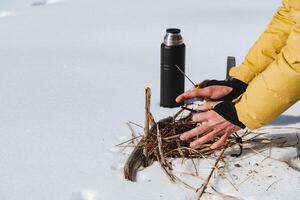 Hände warm durch das Feuer, Licht ein Feuer im das Schnee mit ein Feuer, ein Thermosflasche mit Tee, behalten das Finger offen. foto