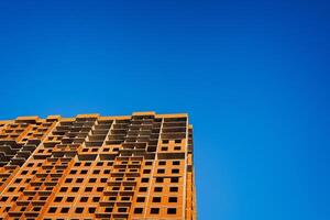 ein Stück von das Gebäude ist unter Konstruktion. das Wände von das Haus sind gefüttert mit rot Ziegel. ein unvollendet Gebäude gegen ein Blau Himmel. foto