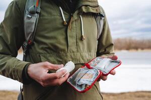 zuerst Hilfe Bausatz, ein einstellen von verschiedene Medikamente gesammelt im ein rot Tasche, Tabletten zum Schmerz, ein elastisch Bandage, ein Mann hält ein Erste Hilfe Kit im seine Hände, Wandern Ausrüstung. foto