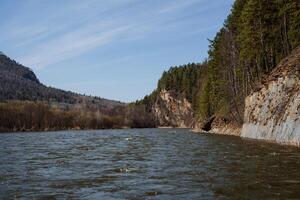 das Fluss fließt unter das Berge, das Felsen sinken in das Wasser, das Taiga Fluss im das Herz von Russland, Frühling Tag klar Himmel, das Schönheit von das Blau Himmel, das Nadelbaum Wald von Kiefer foto