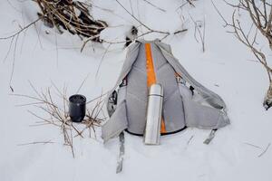 Ausrüstung zum Wandern im das Winter Wald. Thermosflasche mit Becher. Dinge zu sammeln im ein Rucksack. Winter Reise. foto