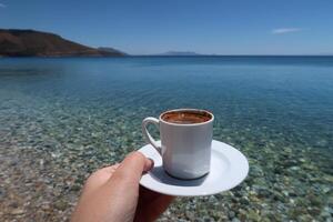 traditionell Türkisch Kaffee Tasse mit Muster. Frau Hand halten das Tasse auf ein sonnig Sommer- Tag, exotisch Meer Hintergrund foto