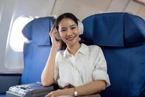 asiatisch jung Frau tragen Kopfhörer Hör mal zu zu Musik- beim zuerst Klasse auf Flugzeug während Flug, Reisen und Geschäft Konzept foto