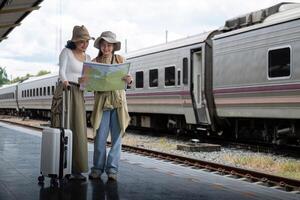 Reise Konzept. Mädchen Freund tragen Hut halten Karte haben Tasche und Gepäck. weiblich Reisender warten Zug beim Zug Bahnhof foto