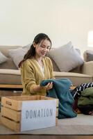 Frau asiatisch halten Spende Box voll mit Kleider und wählen Kleidung. Konzept von Spende und Kleider Recycling. Portion Arm Menschen foto