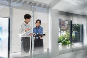 zwei Geschäft asiatisch Menschen lächelnd wie Sie gehen durch ein dokumentieren zusammen im ein Büro foto