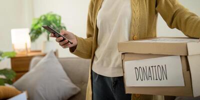 Spende Konzept. Frau asiatisch halten ein spenden Box mit voll von Kleidung. Frau halten Kleider spenden Kasten. Kleider im Box zum Konzept Spende und Wiederverwendung recyceln foto