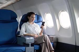 ein Frau ist Sitzung im ein Flugzeug Sitz mit ein Zelle Telefon im ihr Hand foto