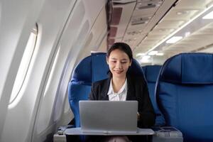 asiatisch jung Frau mit Laptop beim zuerst Klasse auf Flugzeug während Flug, Reisen und Geschäft Konzept foto