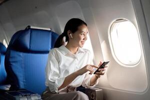 Reisen und Technologie. fliegend beim zuerst Klasse. jung Geschäft Frau Passagier mit Smartphone während Sitzung im Flugzeug Flug foto