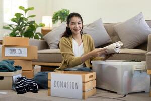 Frau asiatisch halten Spende Box voll mit Kleider und wählen Kleidung. Konzept von Spende und Kleider Recycling. Portion Arm Menschen foto