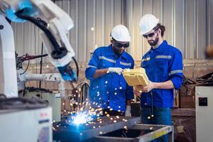 zwei Ingenieure Mechaniker mit Computer Regler Roboter Arm zum Schweißen Stahl im Stahl Fabrik Werkstatt. Industrie Roboter Programmierung Software zum automatisiert Herstellung Technologie . foto