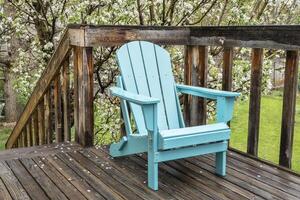 leeren Adirondack Stuhl auf ein hölzern Hinterhof Deck, Frühling Landschaft mit ein Blühen Apfel Baum foto