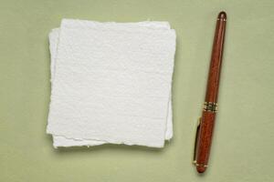 klein Blatt von leer Weiß khadi Lappen Papier mit ein Luxus hölzern Stift gegen Grün Pastell- Hintergrund foto