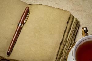 leer retro ledergebunden Tagebuch mit geschmückt Kante handgemacht Papier Seiten mit ein stilvoll Stift und ein Tasse von Tee, Tagebuch schreiben Konzept foto