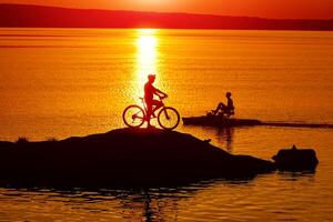 draussen Orange Sonnenlicht von Mann haben ein ausruhen. Sonnenuntergang Silhouette von Sitzung Mann auf ein See. foto