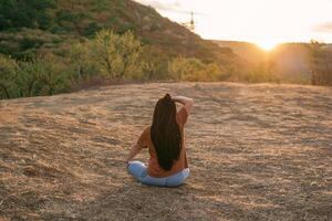 jung Frau ist Sitzung im das Lotus Position und tun Yoga auf Berg Spitze, zurück Sicht. Konzept von gesund Lebensstil. foto