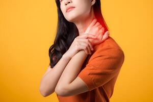 wachsam jung asiatisch Frau im ihr 30er Jahre, tragen ein Orange Shirt, hält ihr Schmerzen Hals auf Gelb Hintergrund. Büro Syndrom Gesundheit Pflege Konzept. foto