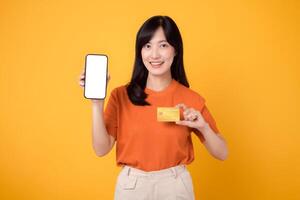 aufgeregt asiatisch Frau im ihr 30er Jahre, präsentieren leer Smartphone Bildschirm und Anerkennung Karte auf beschwingt Gelb Hintergrund. schnell online Zahlung Einkaufen. foto