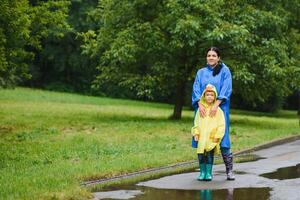 Mama und Sohn im Regenmäntel haben Spaß zusammen im das Regen. Konzept von Familie Ferien und glücklich Kindheit. foto