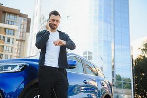 Porträt von ein jung Mann mit ein Handy, Mobiltelefon Telefon im seine Hand in der Nähe von ein Auto auf ein Sommer- Straße. foto