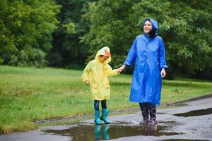 Mutter und Kind, Junge, spielen im das Regen, tragen Stiefel und Regenmäntel foto