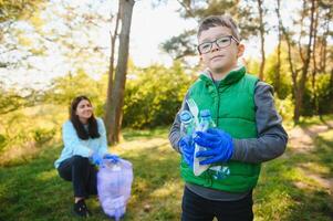 Mama unterrichtet ihr Sohn zu sauber oben Müll im Natur. ein Frau entfernt Plastik Flaschen im ein Tasche. das Thema von Umwelt Verschmutzung durch Müll. foto