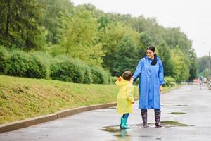 Mutter und Kind, Junge, spielen im das Regen, tragen Stiefel und Regenmäntel foto