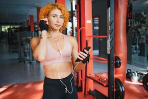 Porträt von jung Sportlerin mit Smartphone Hören zu Musik- im Fitnessstudio. foto