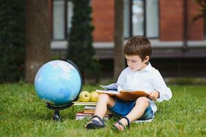 Schüler in der Nähe von Schule. Junge Sitzung mit ein Buch. foto