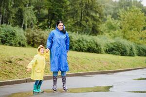 Mutter und Kind, Junge, spielen im das Regen, tragen Stiefel und Regenmäntel foto