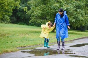 Mama und Sohn im Regenmäntel haben Spaß zusammen im das Regen. Konzept von Familie Ferien und glücklich Kindheit. foto