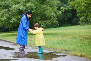 Mama und Sohn im Regenmäntel haben Spaß zusammen im das Regen. Konzept von Familie Ferien und glücklich Kindheit. foto