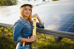 Frauen Ingenieur Arbeiten auf Überprüfung Ausrüstung beim Grün Energie Solar- Leistung Pflanze Überprüfung Solar- Panel und Struktur mit Tablette Checkliste foto