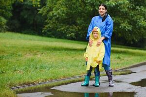 Mutter und Kind, Junge, spielen im das Regen, tragen Stiefel und Regenmäntel foto