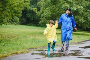 Mutter und Kind, Junge, spielen im das Regen, tragen Stiefel und Regenmäntel foto