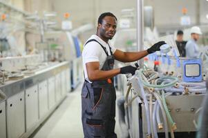 afrikanisch männlich Ingenieur. Steuerung ein Material Produktion Maschine System, Arbeiten im ein Plastik und Stahl Industrie hinsichtlich das Firma Produkt Geschäft. foto