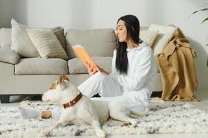 Mädchen lesen ein Buch mit ihr Hund neben ihr. Frau liest ein Buch mit Hund auf das Fußboden foto