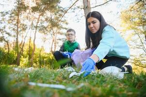 Mama unterrichtet ihr Sohn zu sauber oben Müll im Natur. ein Frau entfernt Plastik Flaschen im ein Tasche. das Thema von Umwelt Verschmutzung durch Müll. foto