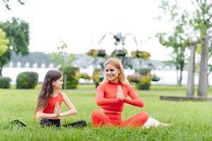 Mutter und Tochter tun Yoga Übungen auf Gras im das Park beim das Tag Zeit foto