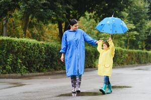 Mutter und Kind, Junge, spielen im das Regen, tragen Stiefel und Regenmäntel foto