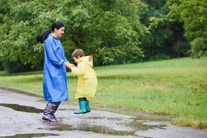 Mama und Sohn im Regenmäntel haben Spaß zusammen im das Regen. Konzept von Familie Ferien und glücklich Kindheit. foto