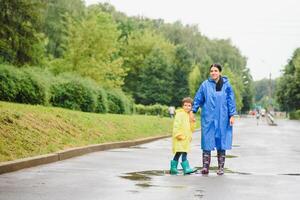 Mutter und Kind, Junge, spielen im das Regen, tragen Stiefel und Regenmäntel foto