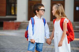 glücklich Kinder gehen zurück zu Schule. Schüler von primär Schule gehen Studie mit Rucksack draußen. Kinder gehen Hand im Hand. Anfang von Unterricht. zuerst Tag von fallen. Junge und Mädchen von elementar Student. foto