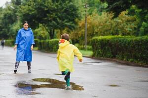 Mama und Sohn im Regenmäntel haben Spaß zusammen im das Regen. Konzept von Familie Ferien und glücklich Kindheit. foto